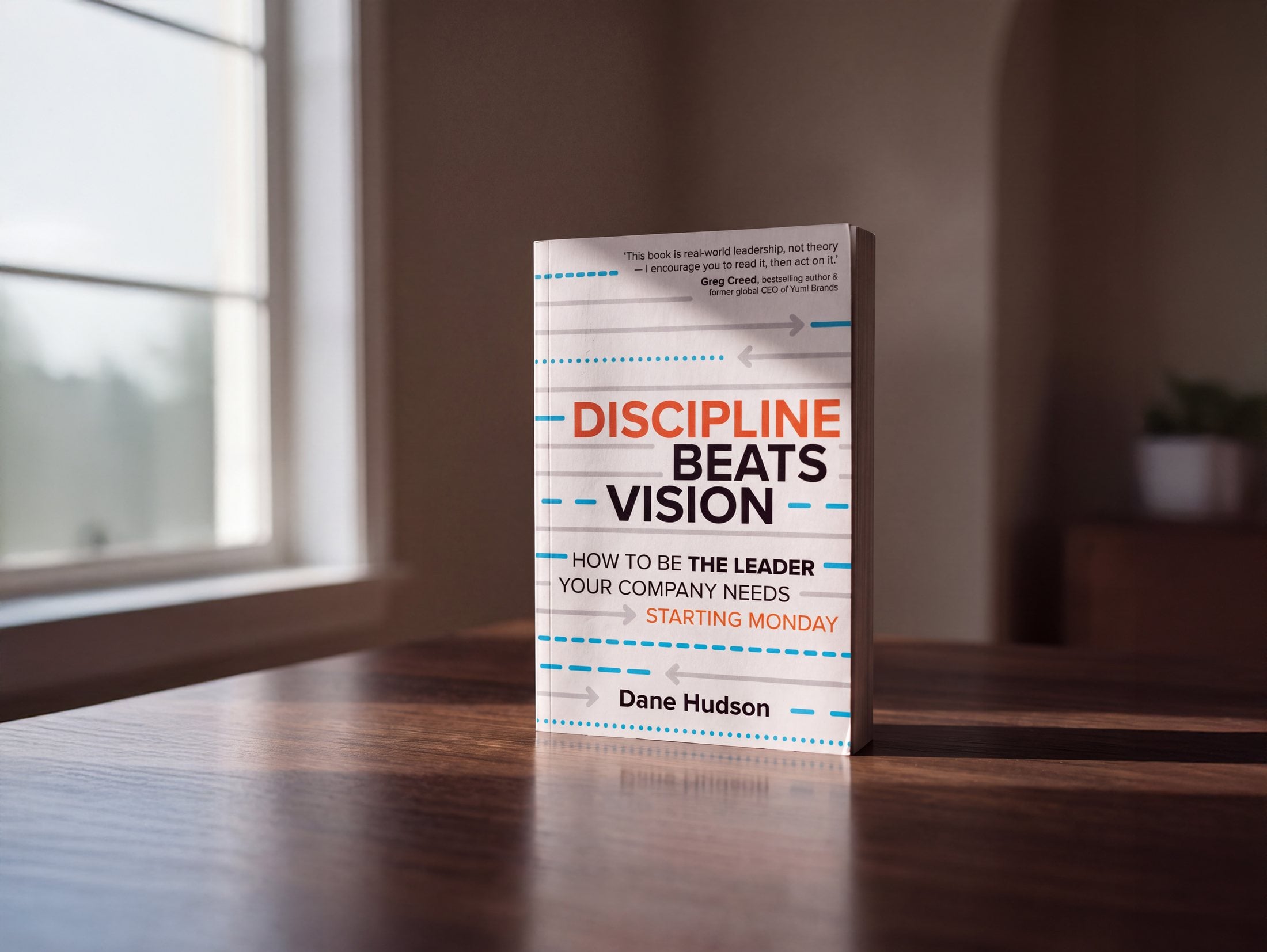 The book Discipline Beats Vision standing on a wooden table beside a sunlit window